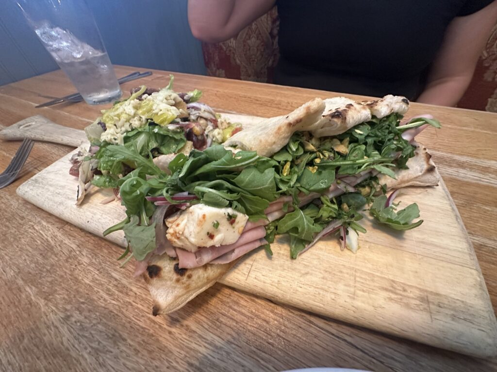 Flatbread panuzzo sandwich with greens, sliced meat, cheese, and side salad at Pizzeria Gusto.