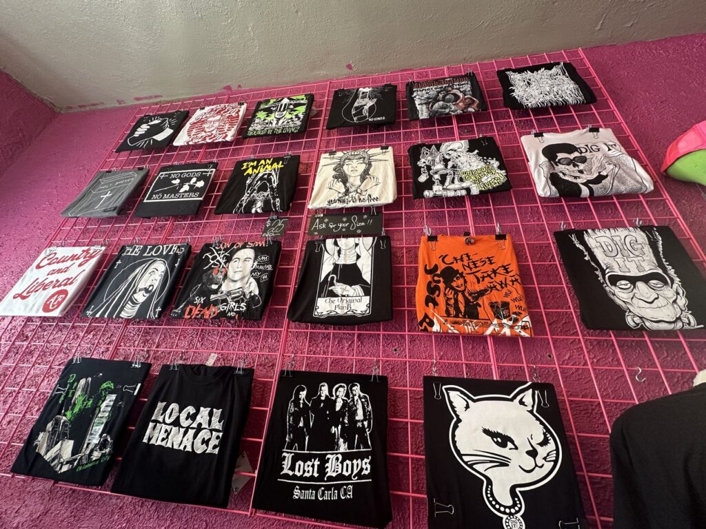 Graphic tote bags with punk and horror designs hanging on a pink wall at Dig It in Oklahoma City.