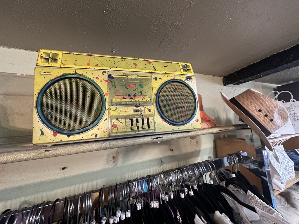Yellow paint-splattered vintage Panasonic boombox displayed above clothing racks at Dig It.