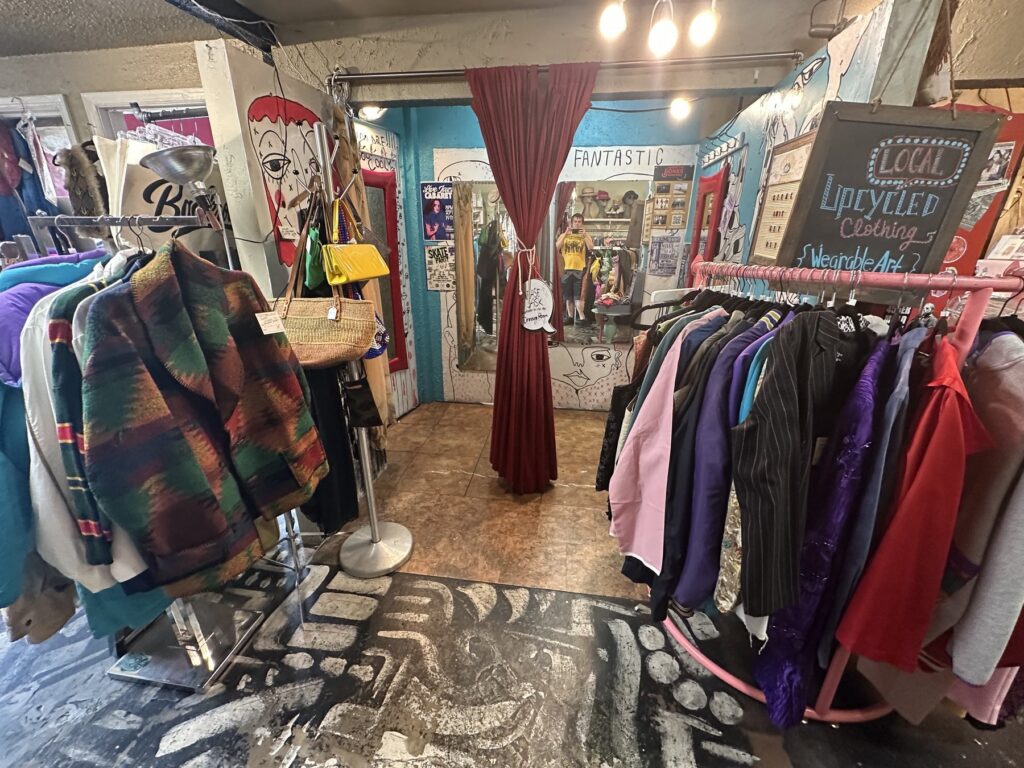 Colorful interior room at Dig It with clothing racks, bags, painted walls, and a local upcycled clothing sign.