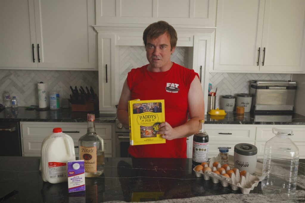 Cook holding the yellow Paddy's Pub cookbook in a kitchen with Fight Milk ingredients on the counter.