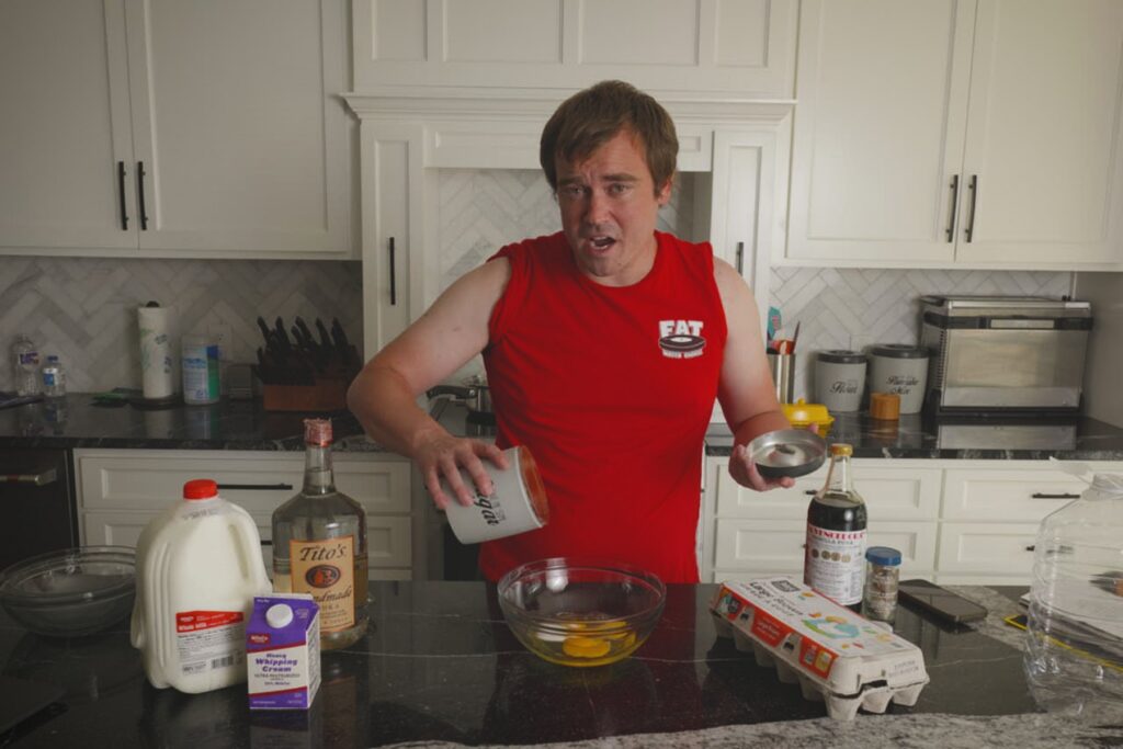 Cook adding sugar to a glass bowl of eggs while making Fight Milk in a home kitchen.