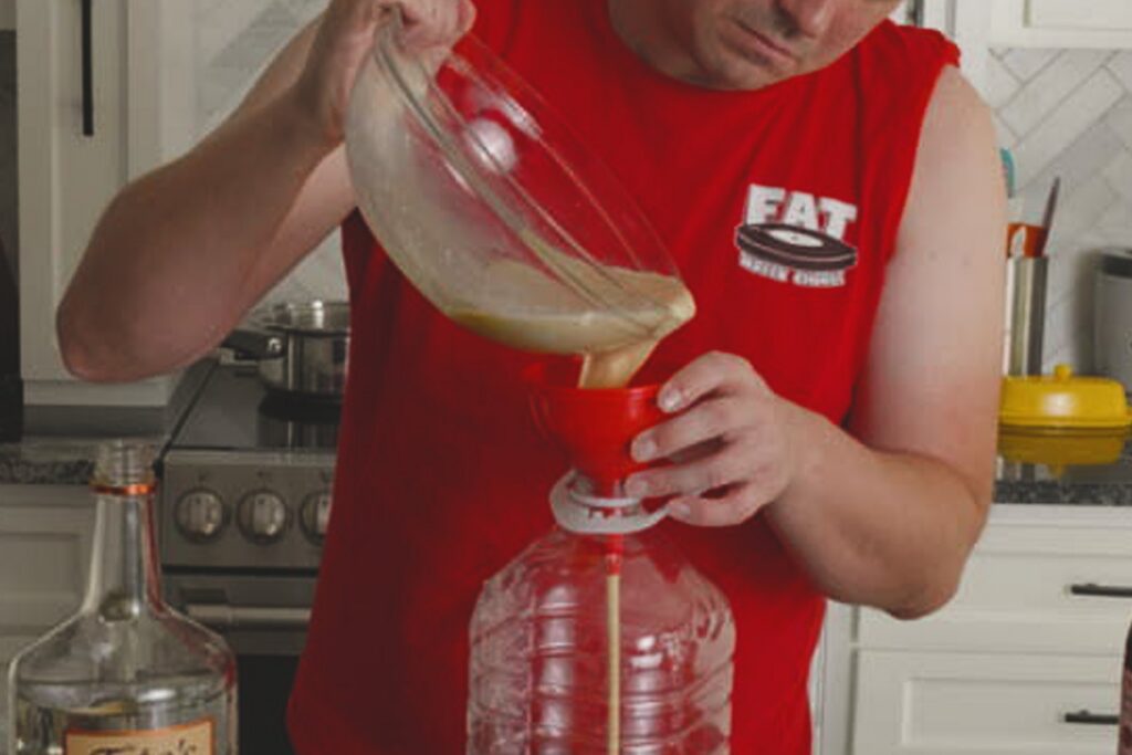 Cook pouring homemade Fight Milk through a red funnel into a large plastic jug.