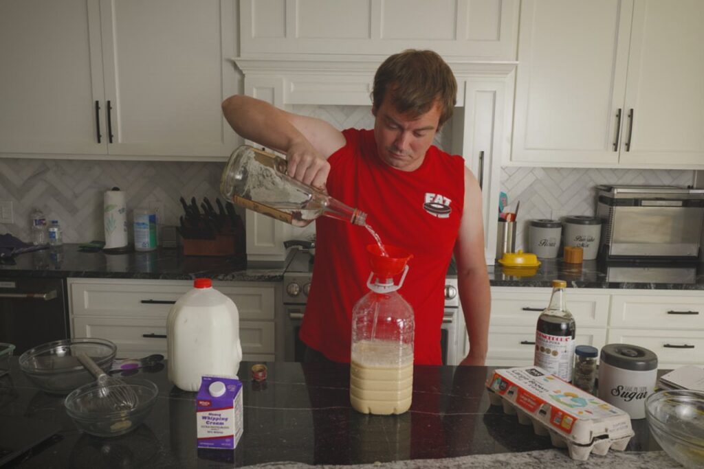 Cook pouring vodka through a red funnel into a large jug of homemade Fight Milk.