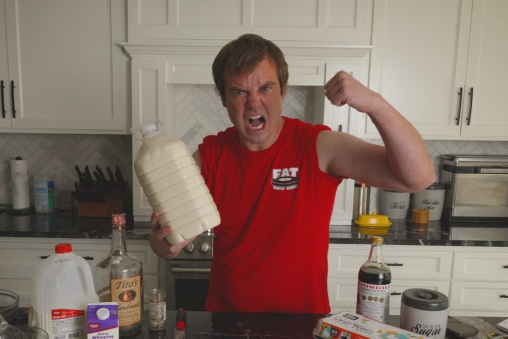 Cook yelling and flexing while holding a large jug of homemade Fight Milk in a kitchen.