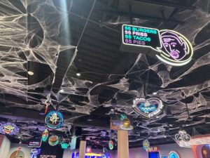 Ceiling at Netflix Bites Dallas covered with spiderweb decor and colorful neon signs for themed food items