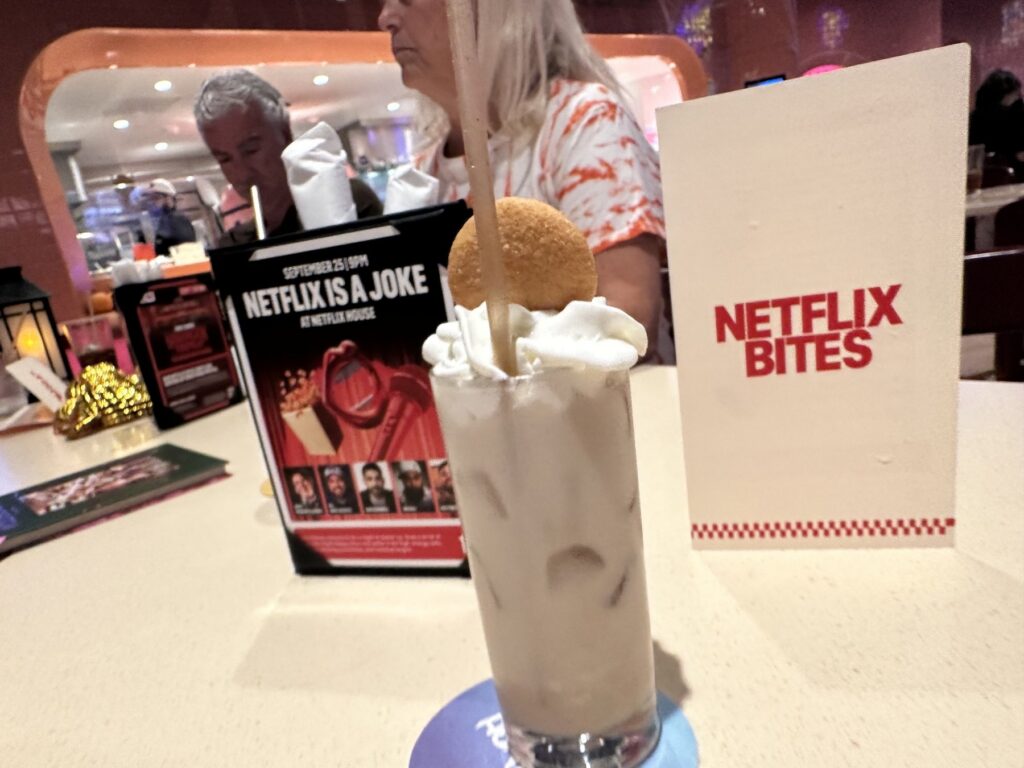 Creamy Netflix Bites Dallas milkshake topped with whipped cream and a cookie beside a Netflix Bites table sign