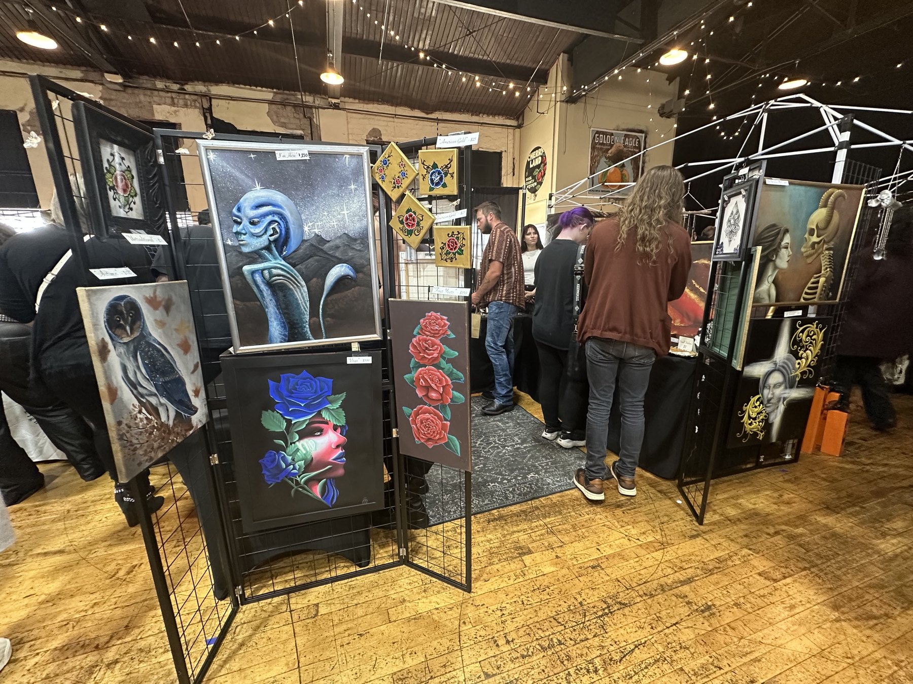 Colorful gothic and surreal paintings displayed on grid panels at the Gothic Market Festival.
