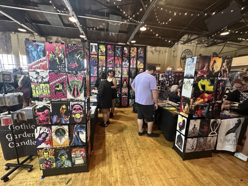 Crowded vendor aisle at the Gothic Market Festival with horror art, candles, prints, and shoppers.
