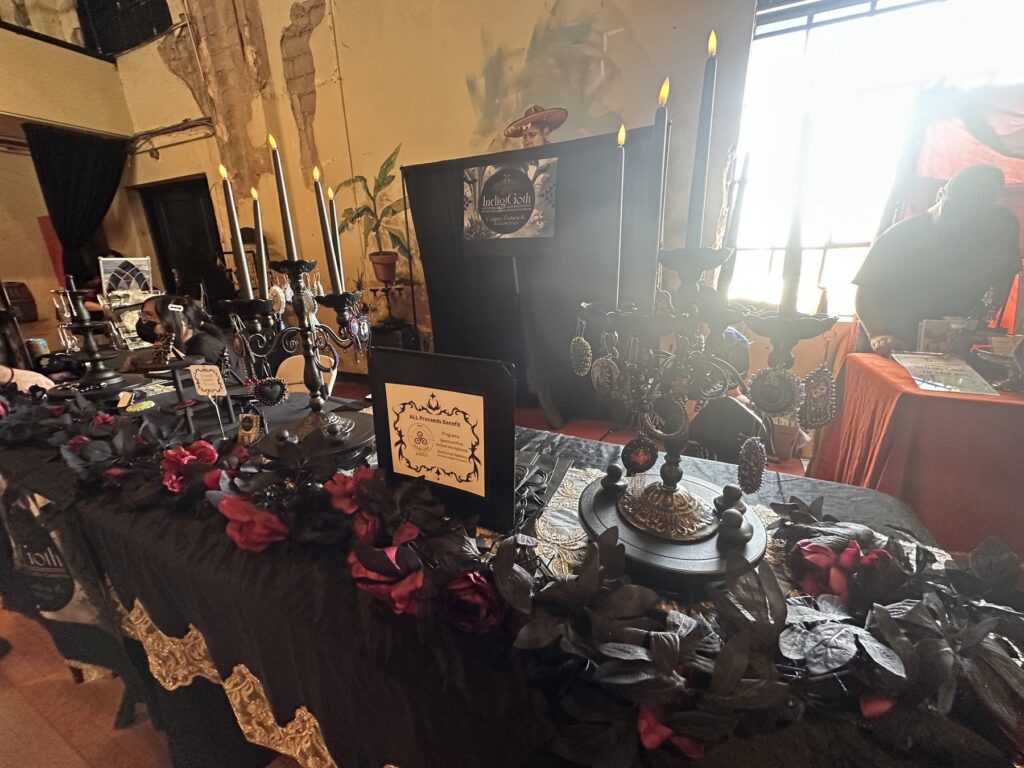 Candlelit gothic vendor display with black flowers, ornate jewelry stands, and dark accessories.