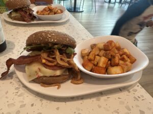 Breakfast burger with bacon, cheese, crispy onions, greens, and seasoned potatoes at Curiosity Cafe.