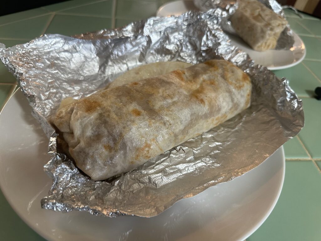 Close-up of an El Taco Express burrito unwrapped in foil on a white plate.