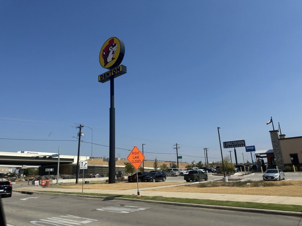 Wide view of the Buc-ee's Denton roadside sign under a blue sky