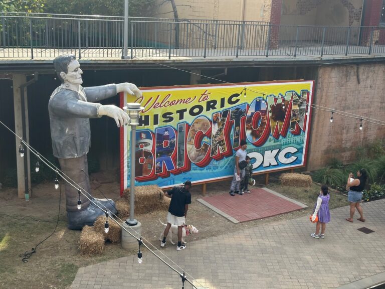 Historic Bricktown OKC welcome sign with a large Frankenstein decoration and families taking photos.