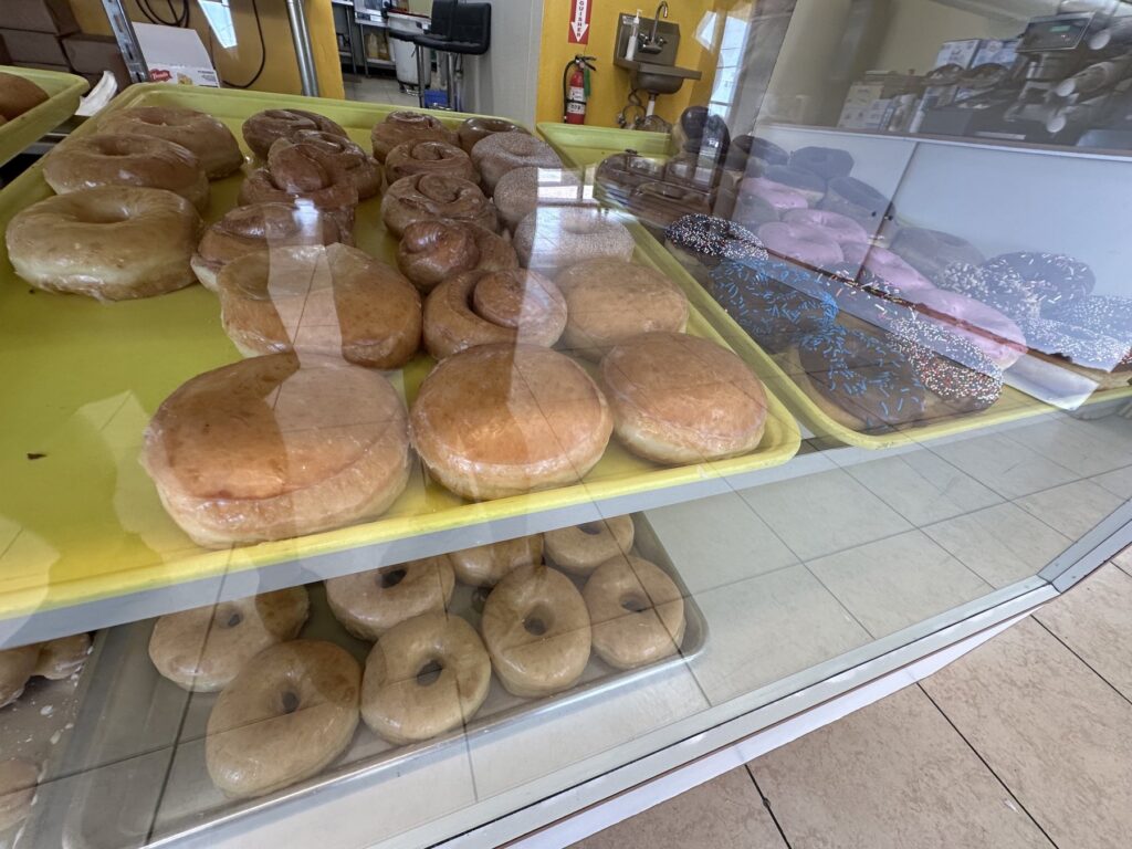 Glazed donuts, cinnamon rolls, pink frosted donuts, and chocolate sprinkle donuts in a bakery case.