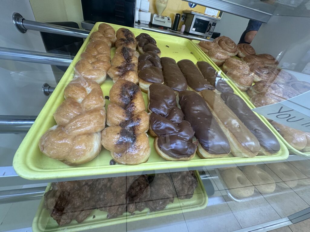 Glazed twists, chocolate long johns, maple bars, and cinnamon rolls displayed in a donut shop case.