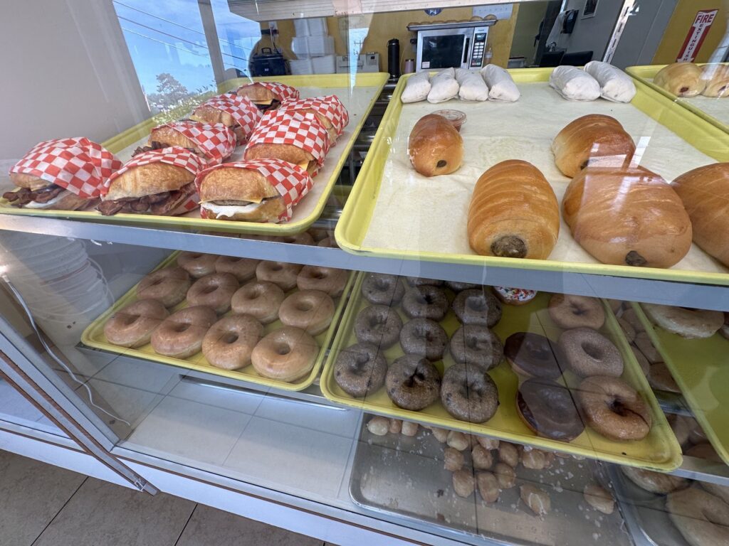 Bakery case with breakfast sandwiches, glazed donuts, filled pastries, chocolate donuts, and donut holes at an Oklahoma donut shop.