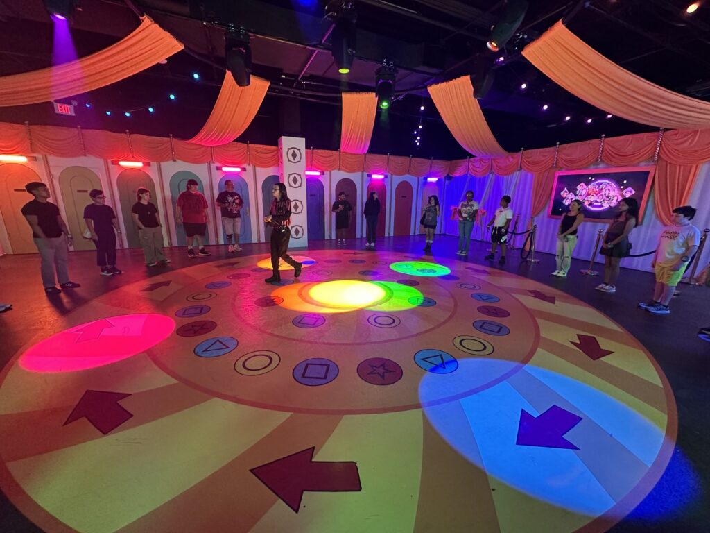 Participants standing around a colorful circular Squid Game challenge floor inside Netflix House Dallas.