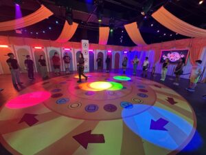 Participants standing around a colorful circular Squid Game challenge floor inside Netflix House Dallas.