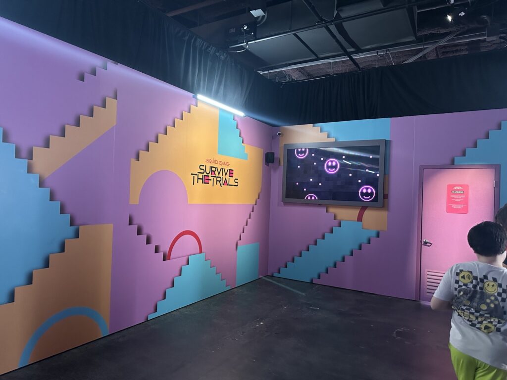 Pastel geometric Squid Game: Survive the Trials wall and screen inside Netflix House Dallas.
