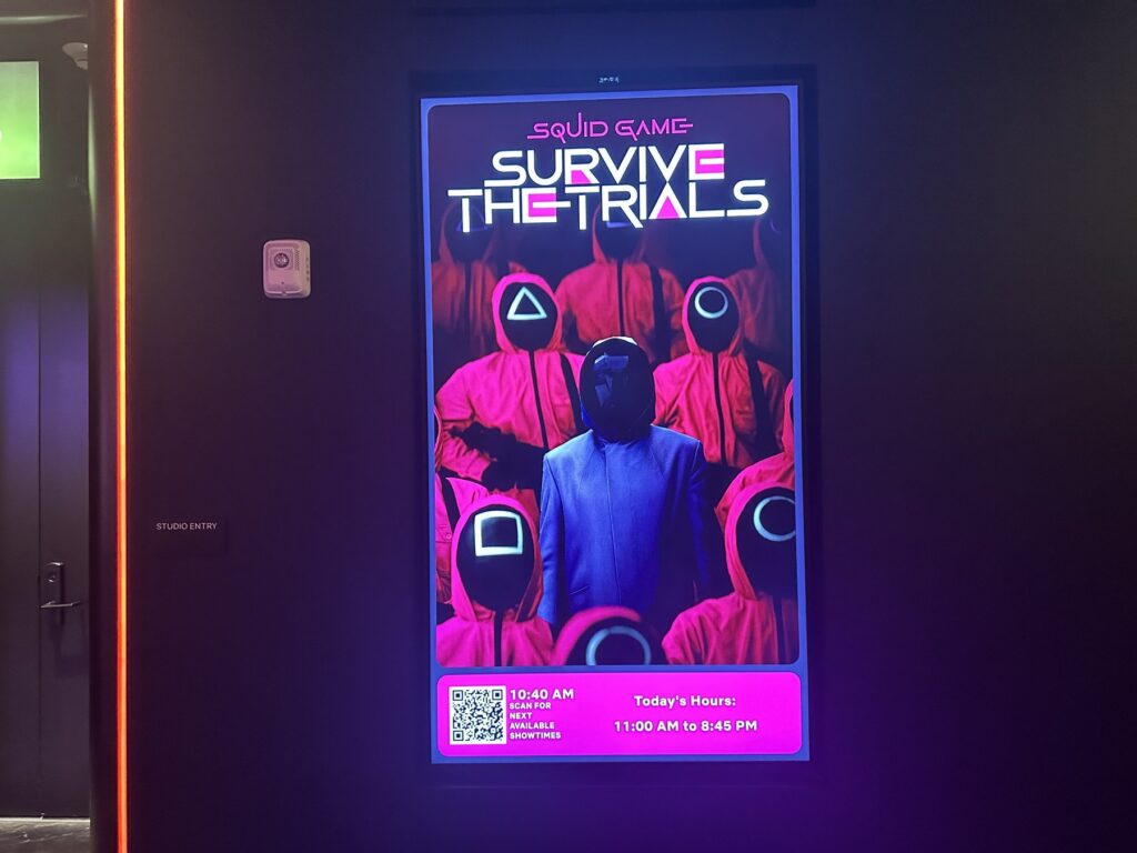 Digital poster for Squid Game: Survive the Trials at Netflix House Dallas with masked guards and showtime information.