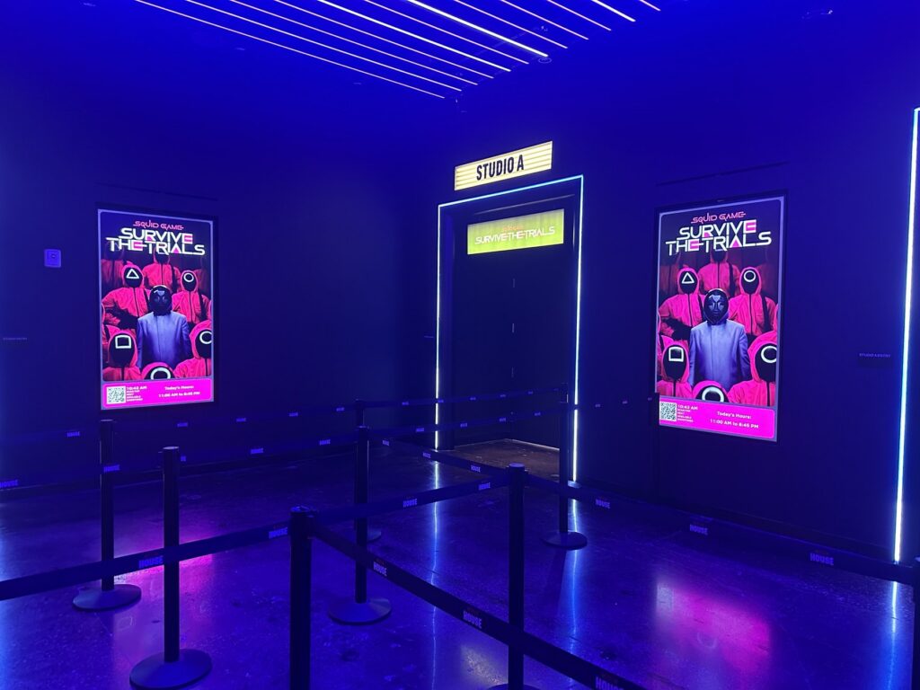 Studio A entrance at Netflix House Dallas with blue lighting and Squid Game: Survive the Trials posters.