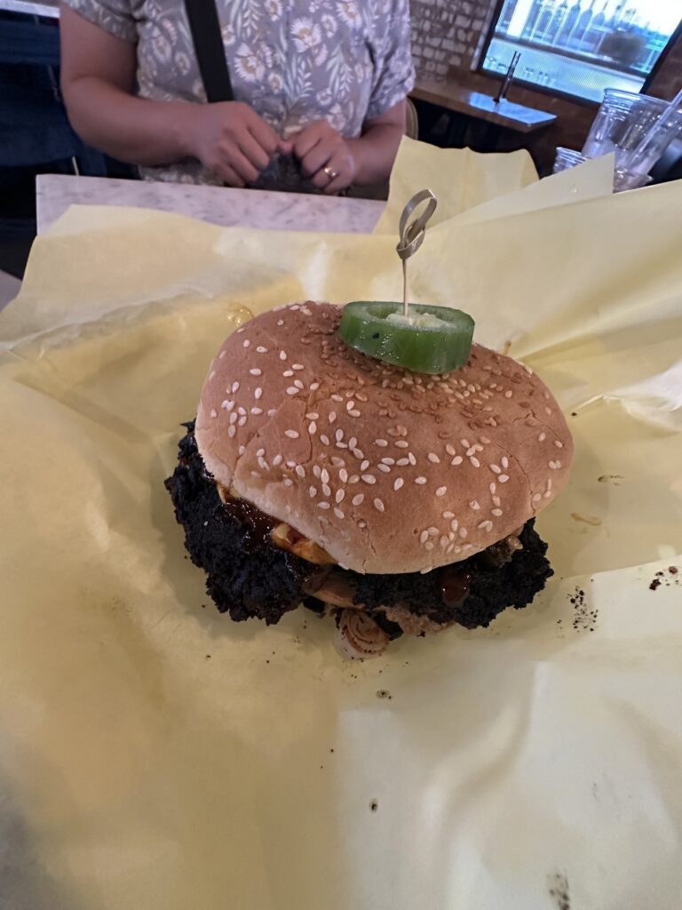 Plant based burger from Enoki Eatz in Oklahoma City served on yellow wrapping paper with a jalapeno slice on top.