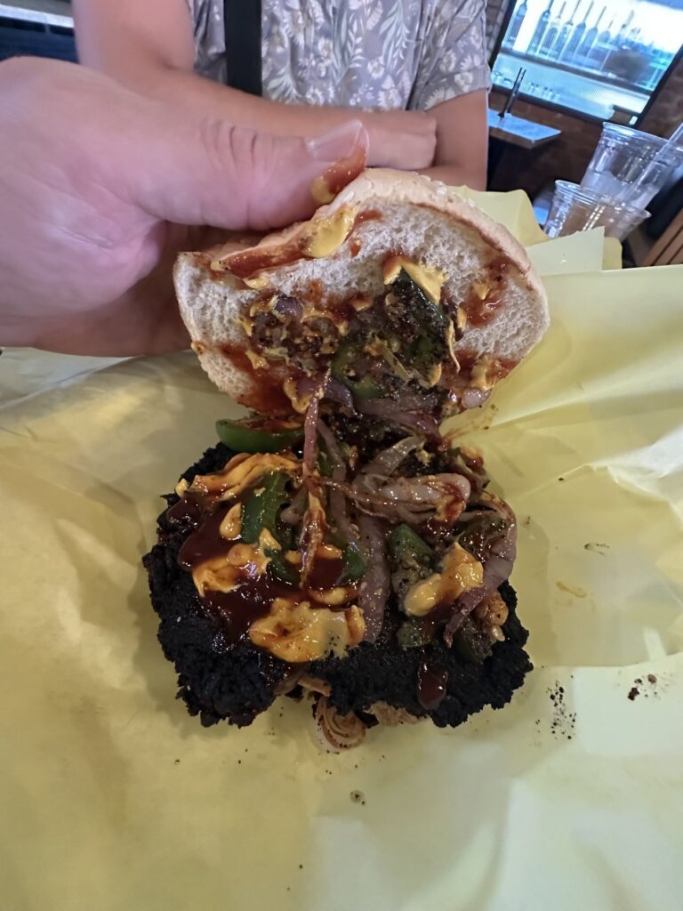 Open plant based burger from Enoki Eatz showing saucy toppings, onions, peppers, and a crispy patty.