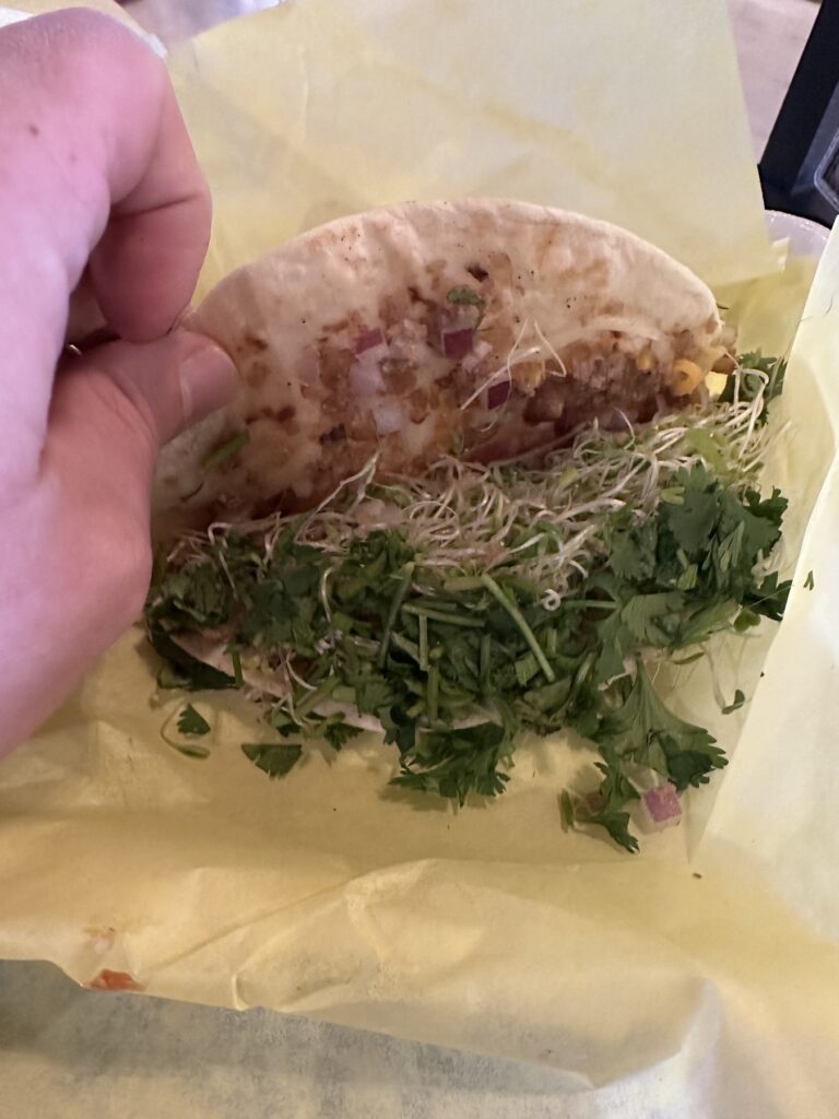 Close-up of a plant based taco from Enoki Eatz with sprouts, cilantro, red onion, and filling.