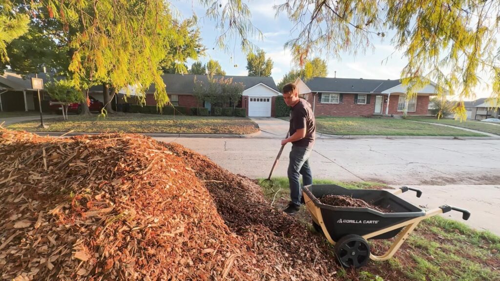 Lance moves wood-chip mulch from a large ChipDrop pile with a wheelbarrow.