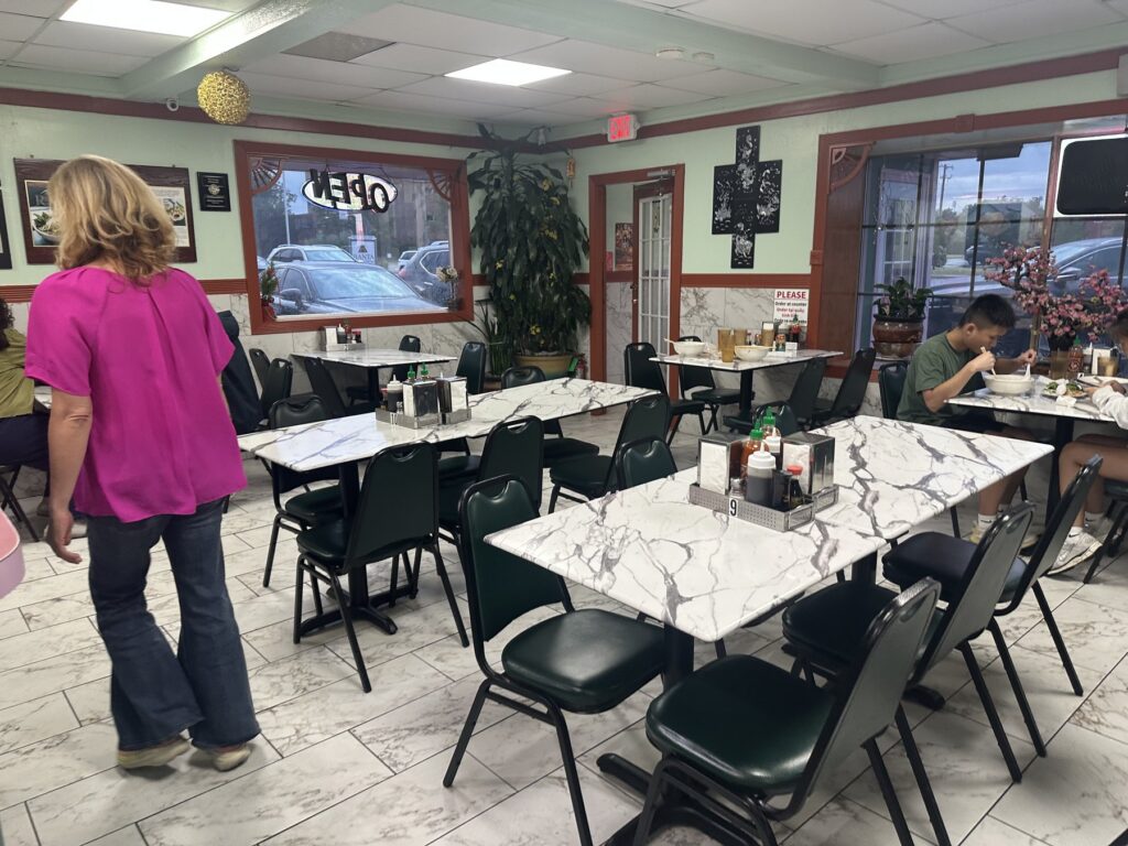 Dining room inside Pho Cuong with marble-look tables, green chairs, condiments, and customers eating.