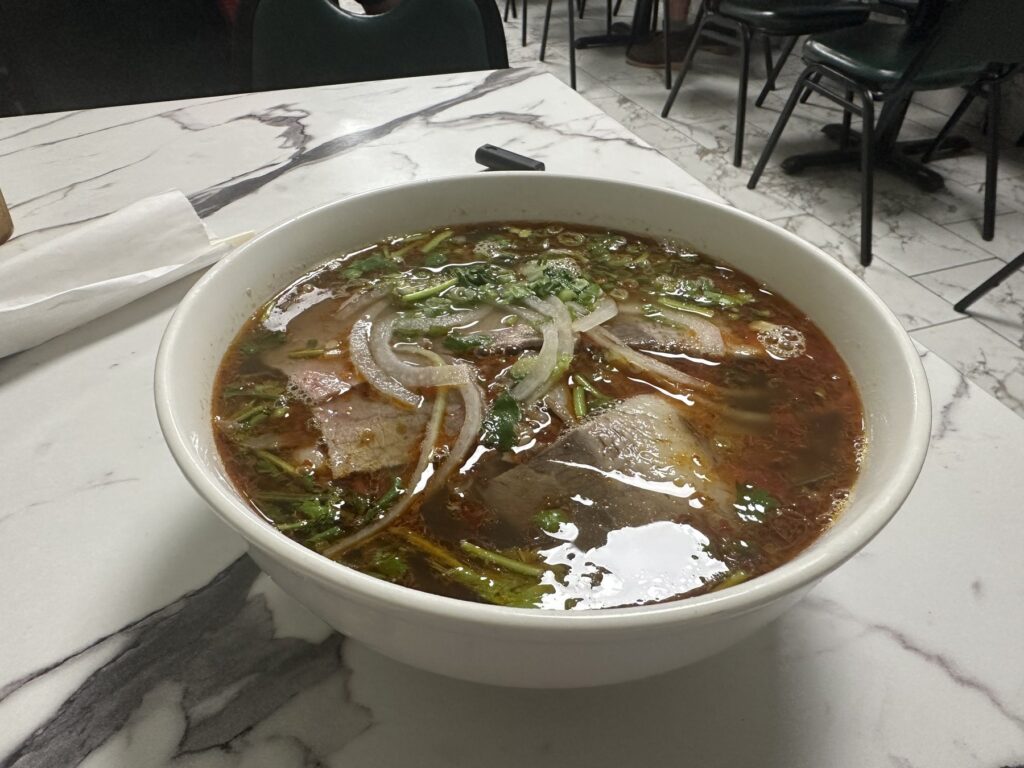Large bowl of Vietnamese noodle soup with sliced meat, onions, herbs, and rich broth at Pho Cuong.