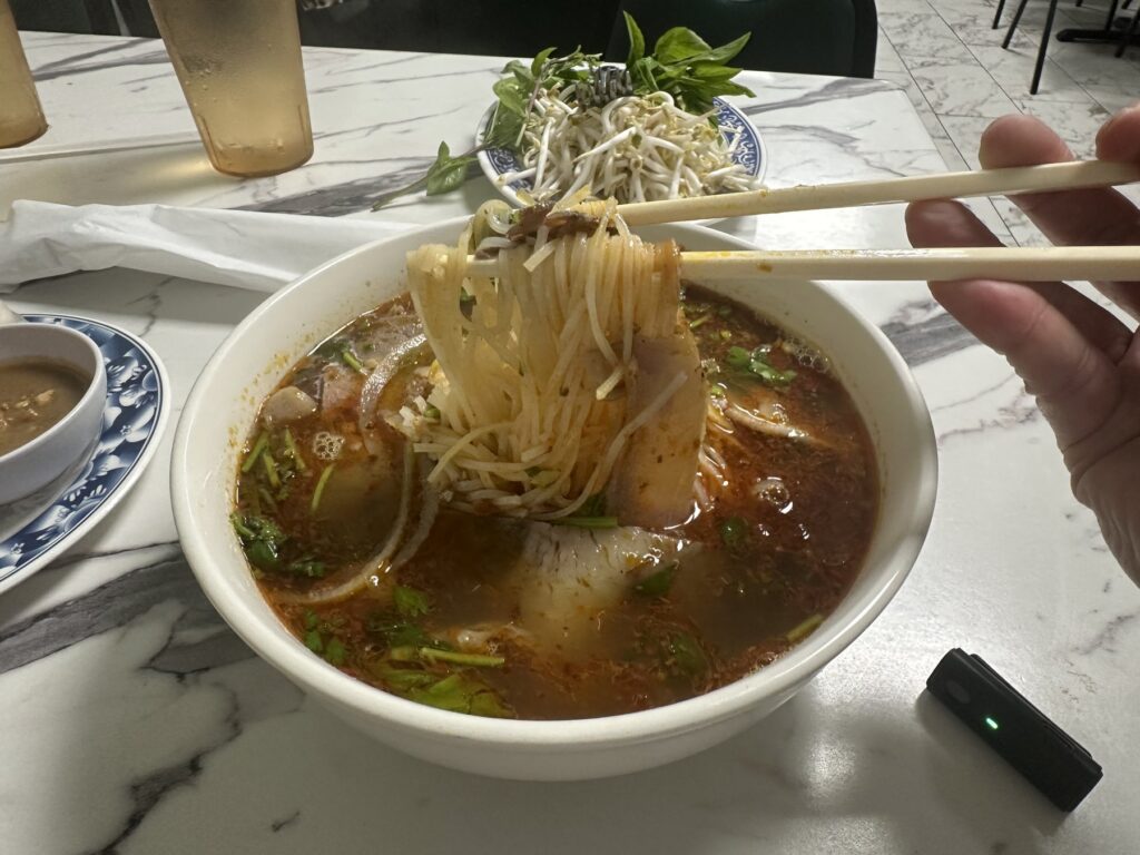 Chopsticks lifting noodles and meat from a bowl of Vietnamese noodle soup at Pho Cuong.