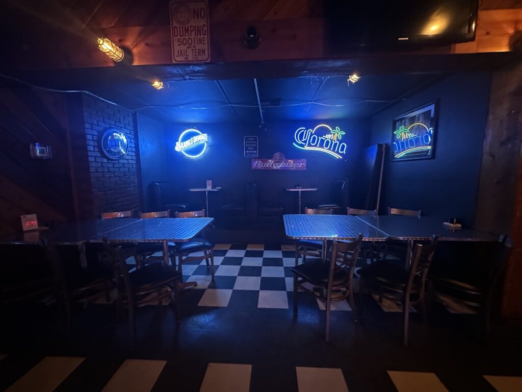 Neon-lit seating area inside JR’s Pub and Grill with tables, booths, and checkered floors.