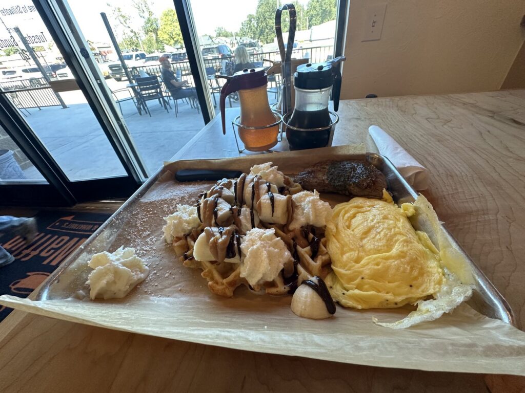 Tray at Just Wafflin’ with an Elvis-style waffle, steak, eggs, whipped cream, bananas, and syrup dispensers