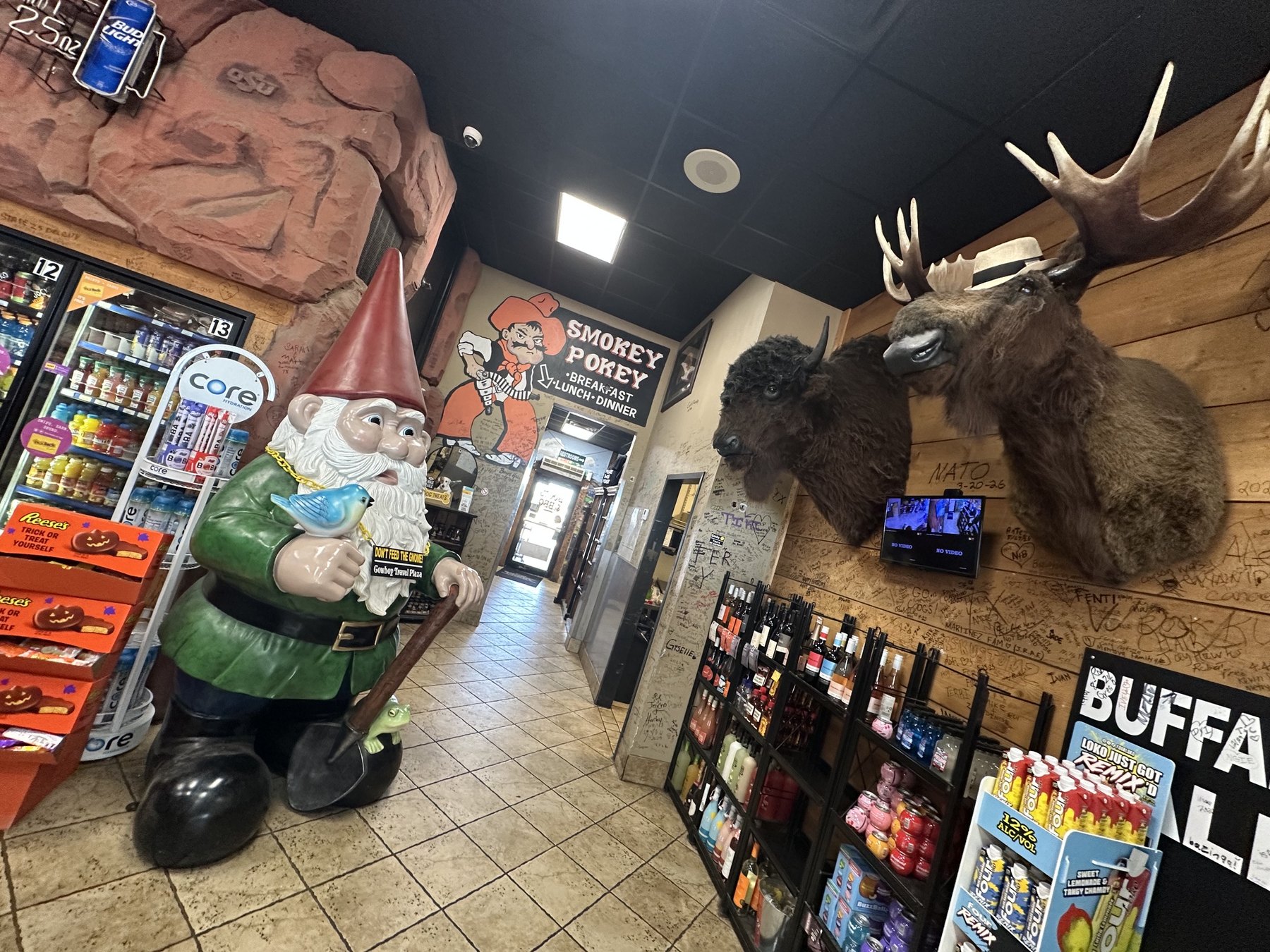 Interior of Cowboy Travel Plaza with a garden gnome statue, mounted animal heads, and Smokey Pokey signage