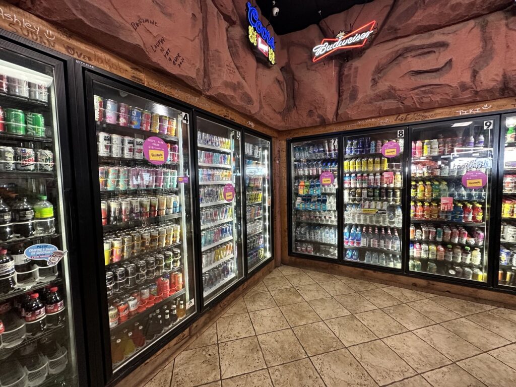 Beverage coolers inside Cowboy Travel Plaza with themed rock walls and neon signs