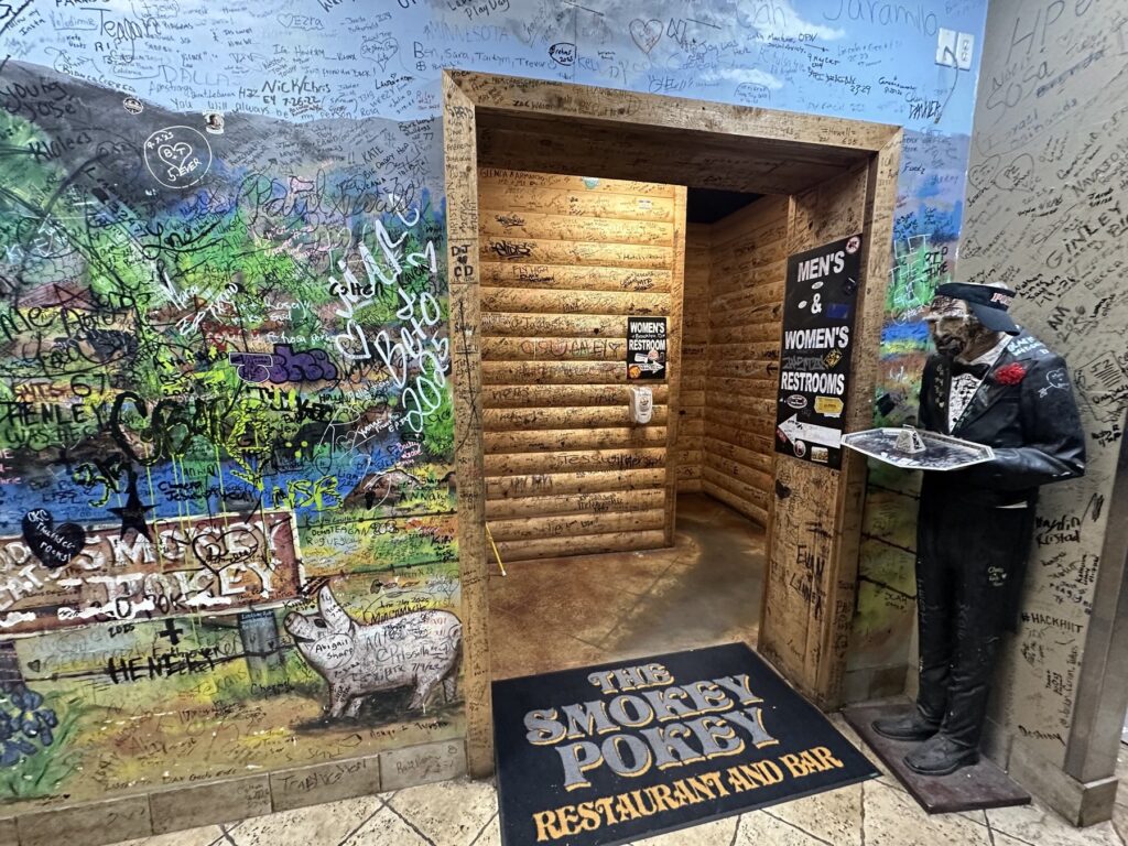 Graffiti-covered restroom hallway inside Cowboy Travel Plaza with Smokey Pokey floor mat and statue