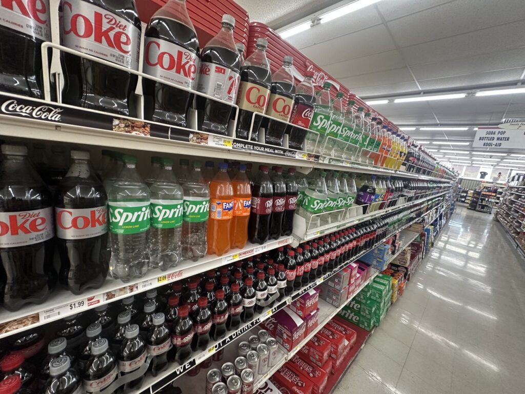 Long soda aisle inside Sweis Foods stocked with Coca-Cola, Sprite, Fanta, and other soft drinks