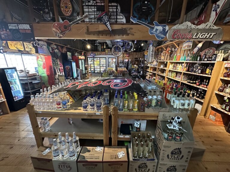 Interior of The Barn liquor store in Stillwater with bottles, coolers, wooden shelves, and beer signs.