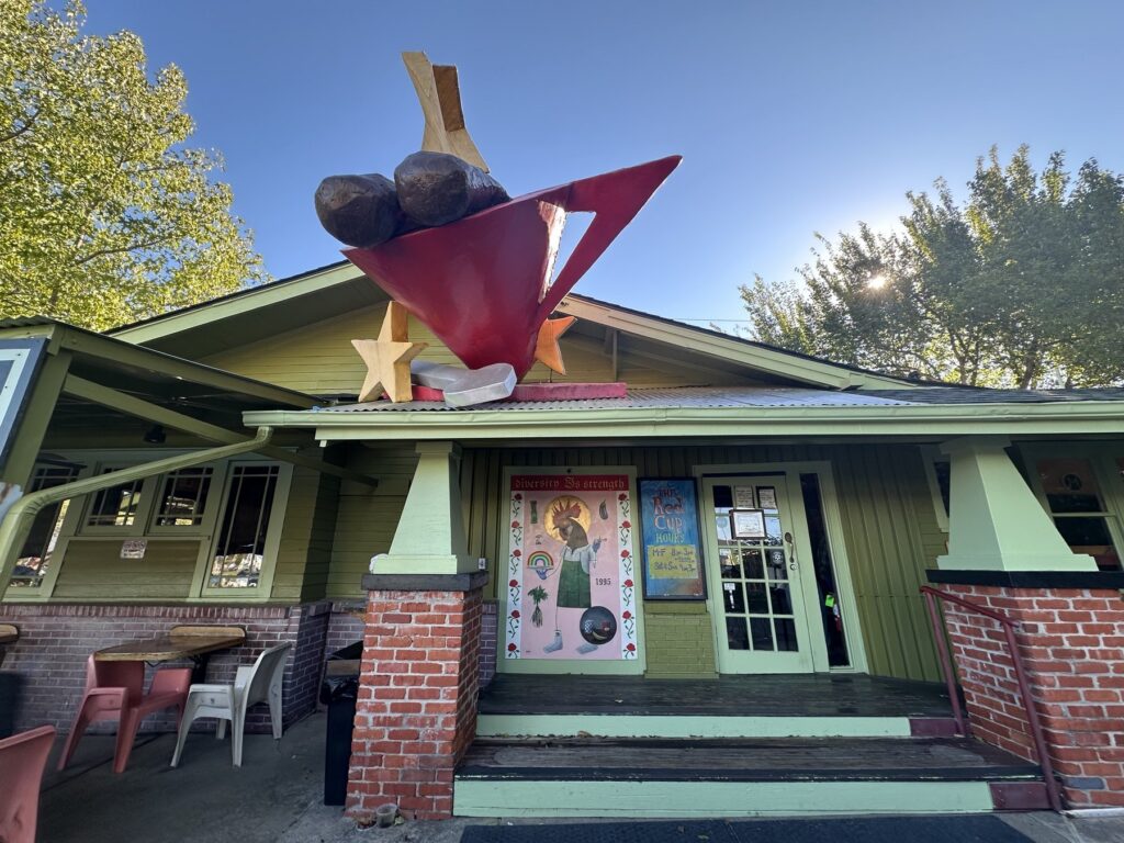Front entrance of The Red Cup in OKC with painted artwork and a rooftop sculpture.