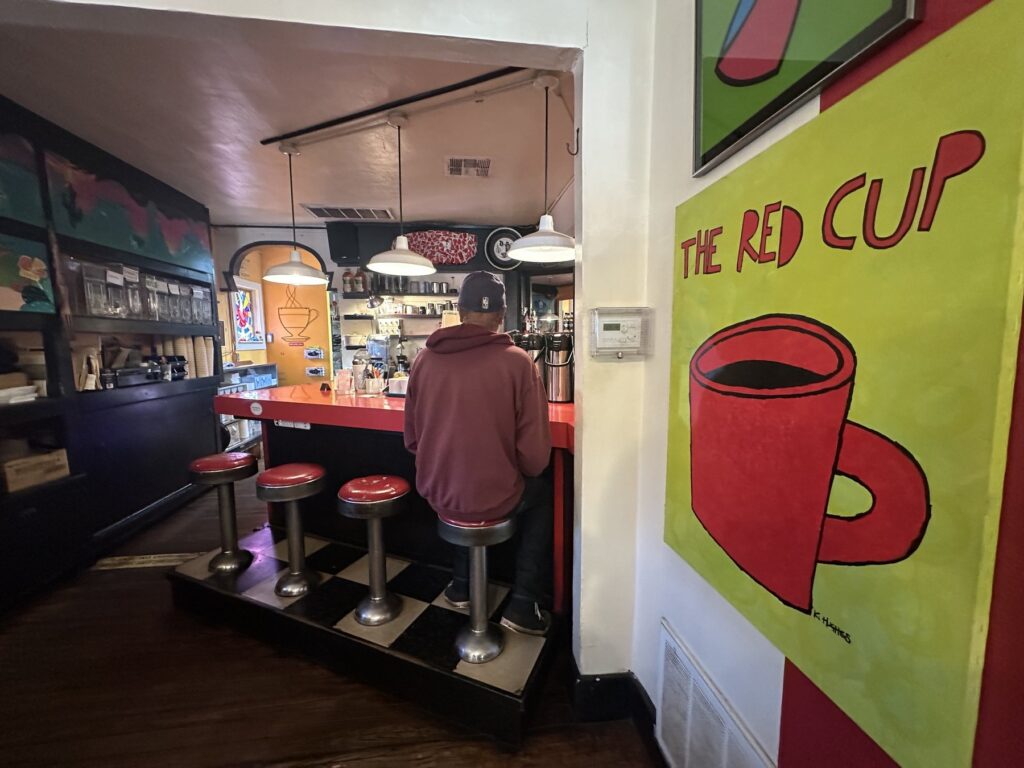 Coffee bar inside The Red Cup in OKC with red stools and a large Red Cup wall painting.