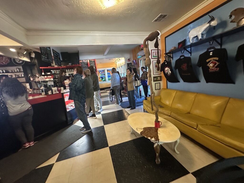 Interior counter area at The Red Cup in OKC with a yellow couch, checkerboard floor, art, and merchandise.