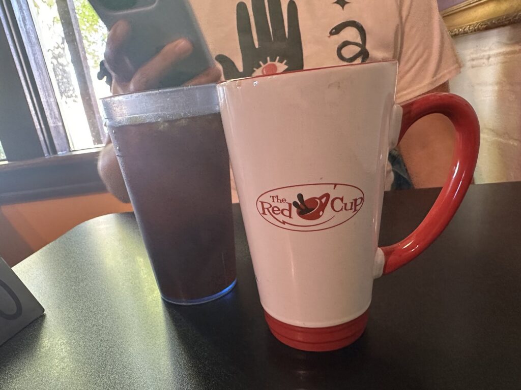 White Red Cup branded coffee mug with a red handle next to an iced drink at The Red Cup in OKC.