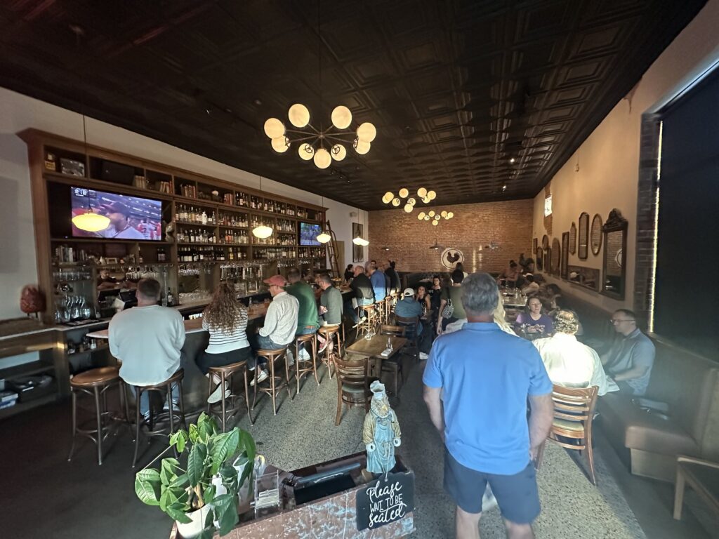 Busy bar and dining room inside Red Rooster in Oklahoma City with brick walls and globe lights.