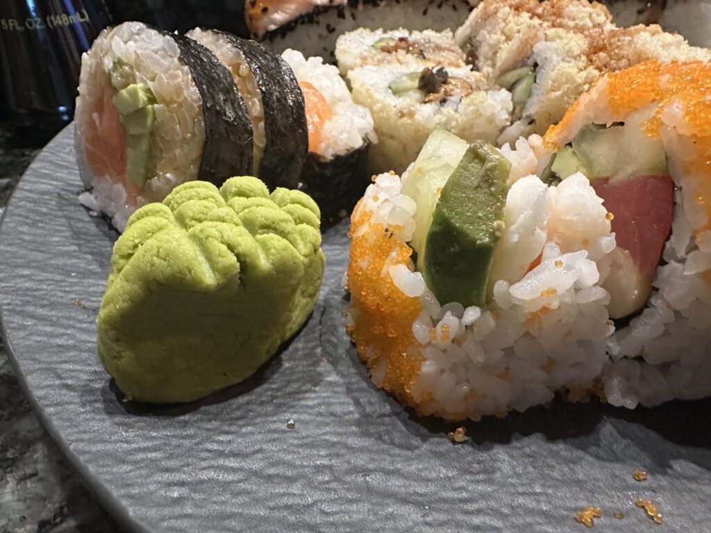 Close-up of assorted Sushi Neko rolls with wasabi on a dark plate.