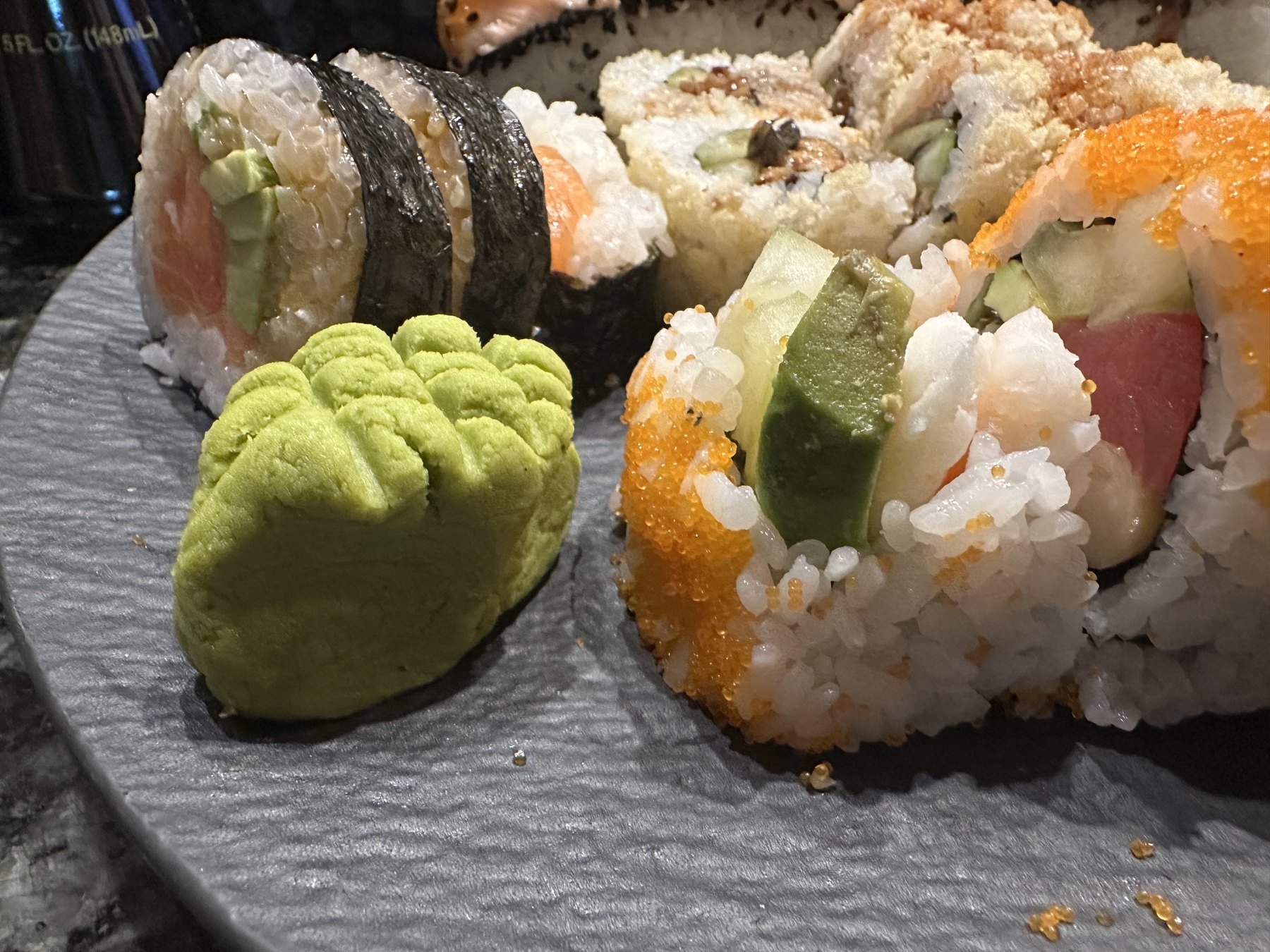 Close-up of assorted Sushi Neko rolls with wasabi on a dark plate.