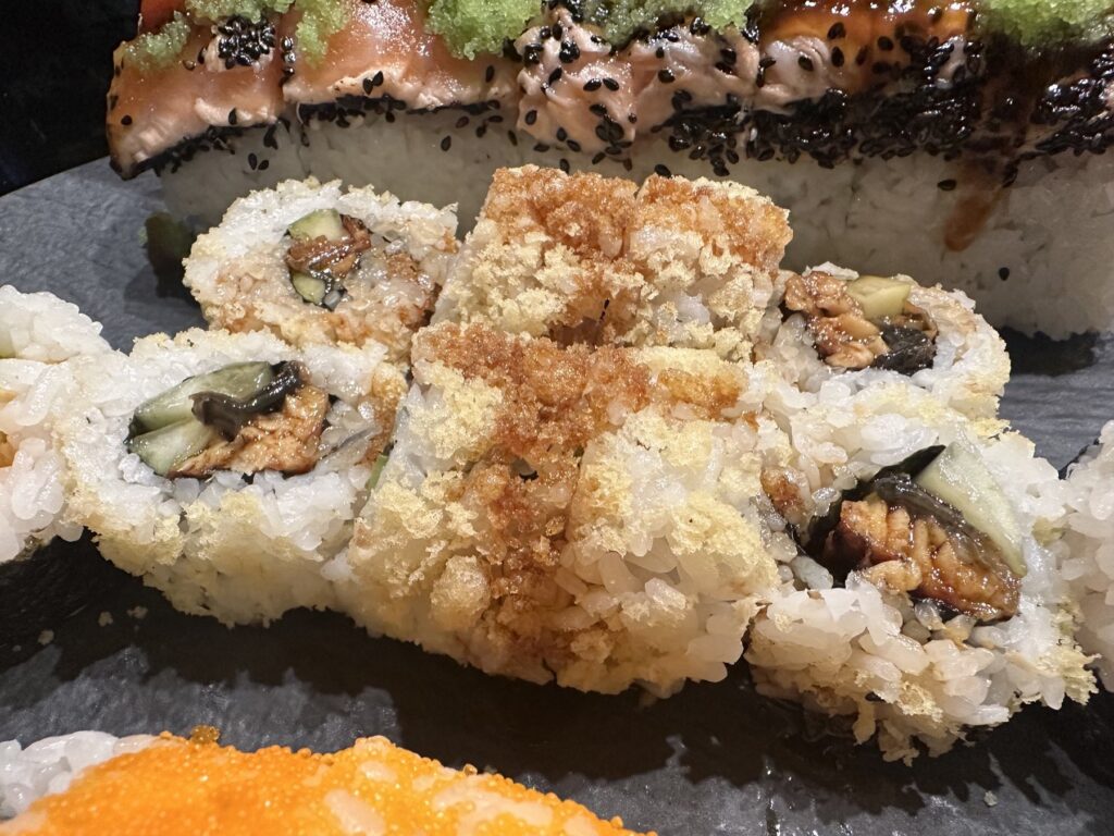 Crunch-topped sushi rolls with a salmon-topped roll behind them at Sushi Neko.
