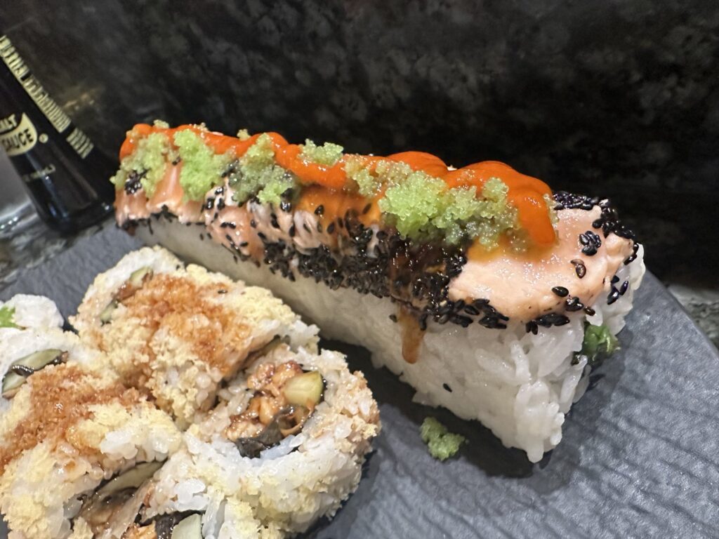 Salmon-topped specialty sushi roll with sesame, roe, and sauce at Sushi Neko.