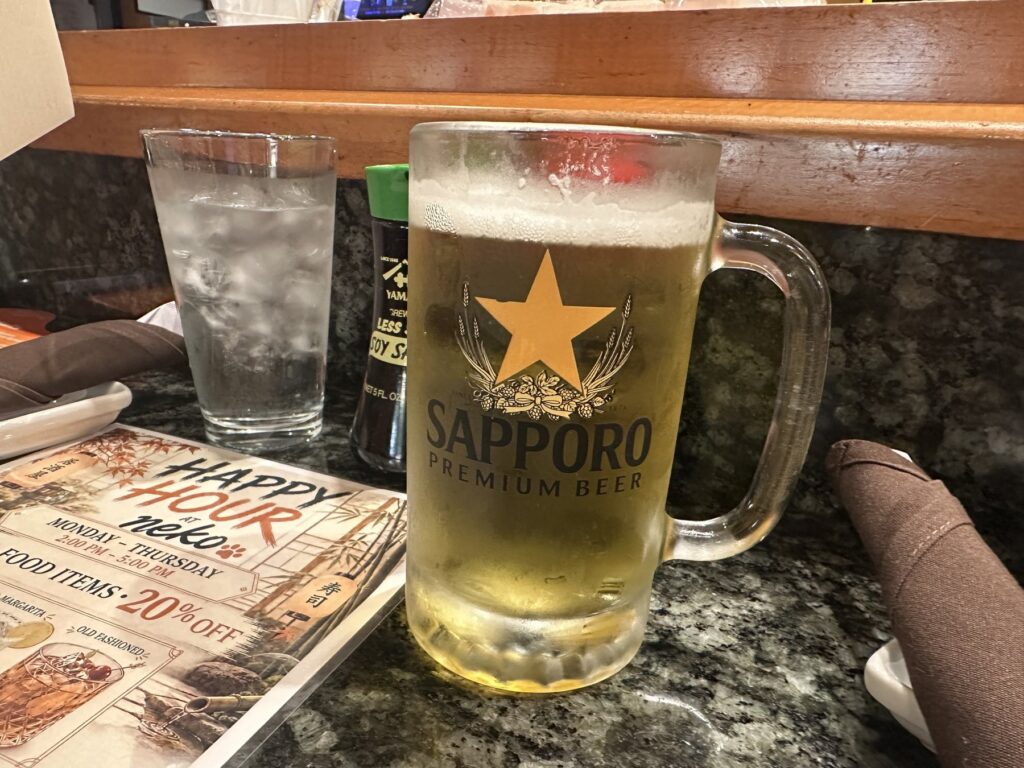 Sapporo beer mug on the bar at Sushi Neko beside a happy hour menu.